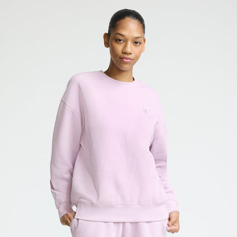 A person stands against a plain background, wearing the Champion Powerblend Crewneck with a small "C" logo and matching sweatpants—hands in pocket and a slight smile for an easy, everyday comfort look.