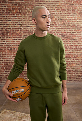 Man in green outfit holding a basketball against a brick wall.