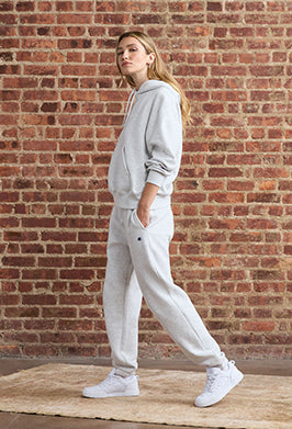 Person wearing a gray sweatshirt and pants standing against a brick wall.